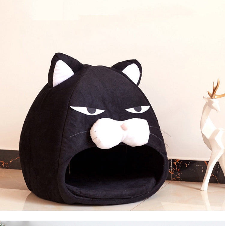 Black pet bed shaped like a cat face on a light wooden floor.