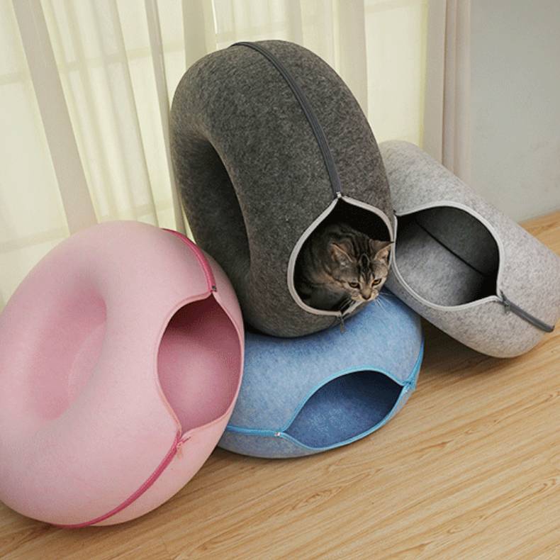 Three pet bed caves in gray, pink, and blue on a wooden floor.