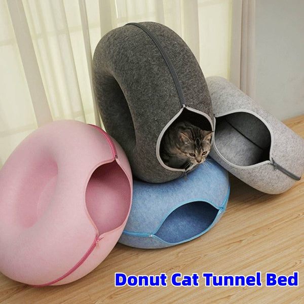 Donut cat tunnel bed in gray, pink, and blue on a wooden surface with a curtain background.